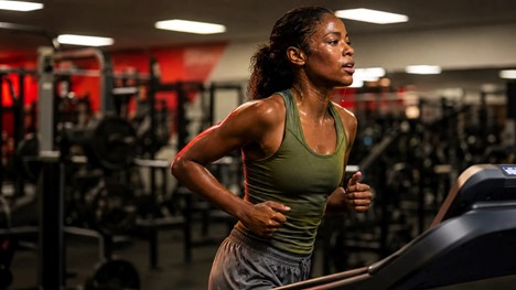 A visibly athletic woman mid-sprint on a treadmill, face caught in genuine mid-effort, embodying the idea that real fitness challenges demand real exertion — the most kinetic, high-energy image in the set.