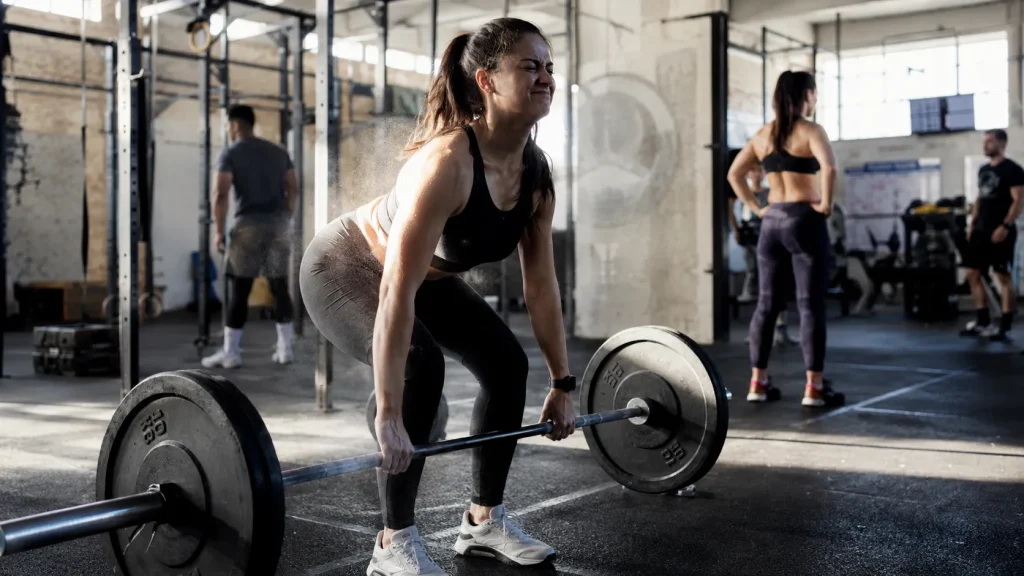 Woman performing a heavy barbell deadlift in a gym, showing focus and effort behind fitness gamification psychology