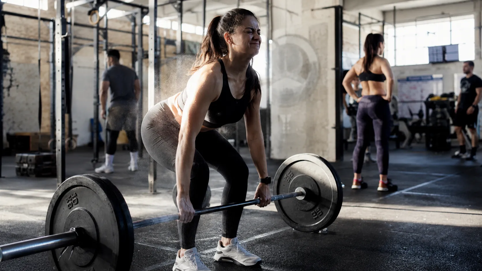 Woman performing a heavy barbell deadlift in a gym, showing focus and effort behind fitness gamification psychology